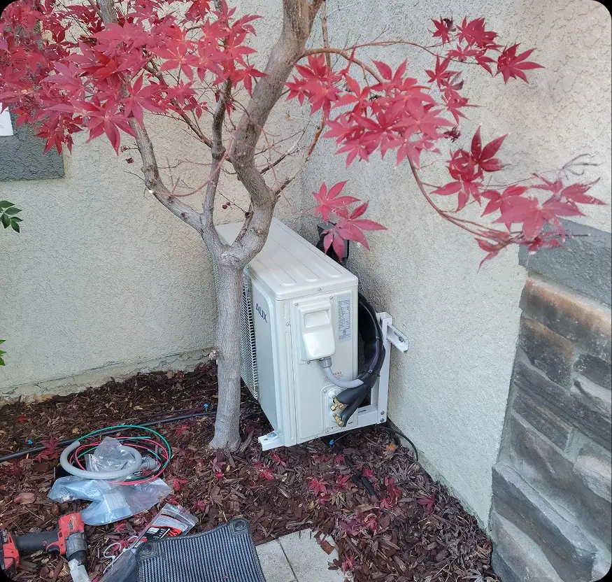 Ductless mini-split installation beside a home with autumn maple tree