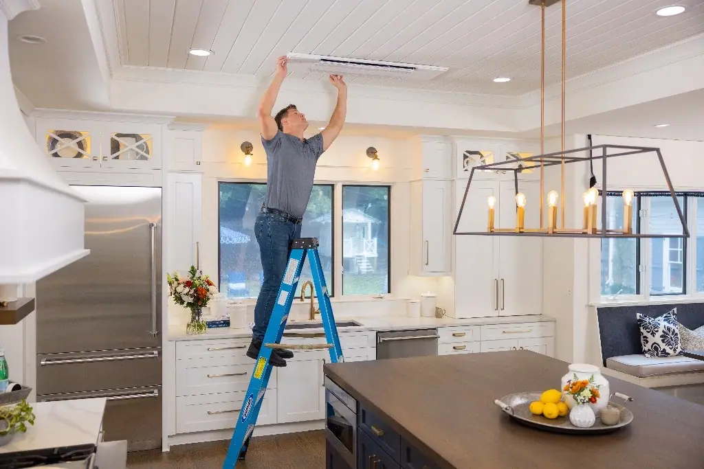 Technician installing a slim ceiling air vent in a bright white kitchen